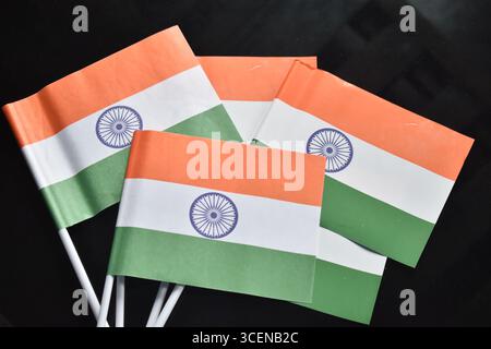 A set of small Indian national flags featuring saffron, white, and green stripes with the Ashoka Chakra, arranged neatly on a dark background. Stock Photo