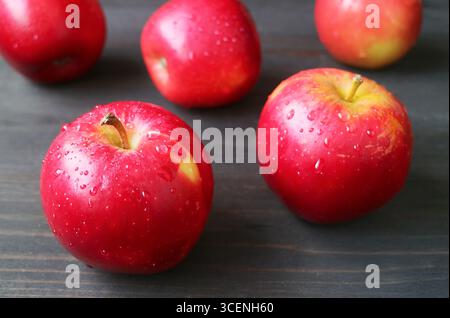 Closeup of red fresh ripe apples with water droplets scattered on black wooden table Stock Photo