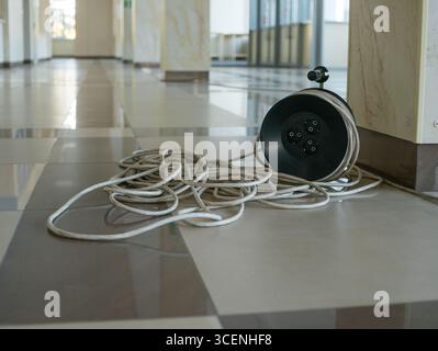 A spool with an unrolled extension cord on the floor in a spacious modern foyer. Stock Photo