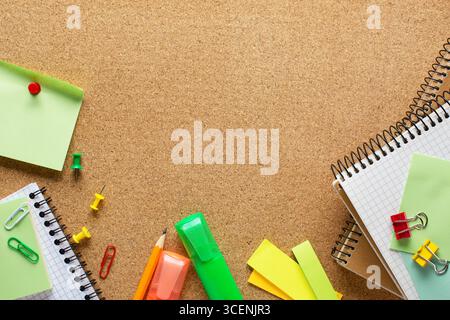 Notepads, markers, pencil, sticky notes, paper sheets, paper clips and binder clips  on cork board  with copy space for text.  Top view of colorful sc Stock Photo