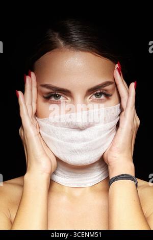 Attractive woman with bandage facial mask posing with glamorous makeup. Perfect brows, eyelashes and fashion look. Plastic surgery and aesthetic Stock Photo