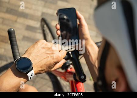 Male cyclist in helmet with mobile phone on bike check apps at park. Space for design. View from above. Close up. Stock Photo