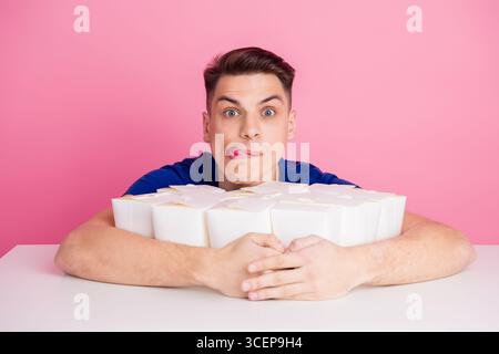 Young man in a blue shirt posing happily with multiple takeout boxes against a vibrant pink background Stock Photo
