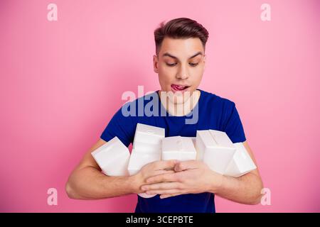 Happy young man holding a stack of white boxes with a playful expression in front of a vibrant pink background Stock Photo