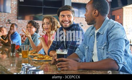 Two Male Friends Sitting At Counter Eating Out In Sports Bar Stock Photo