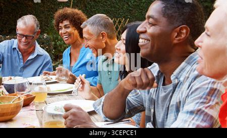 Group Of Mature Friends Sitting Around Table Enjoying Outdoor Meal In Backyard Stock Photo
