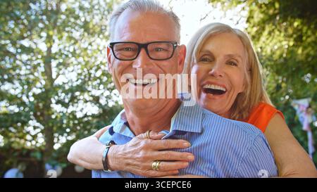 Outdoor Portrait Of Mature Couple With Woman Hugging Man From Behind With Lens Flare Stock Photo