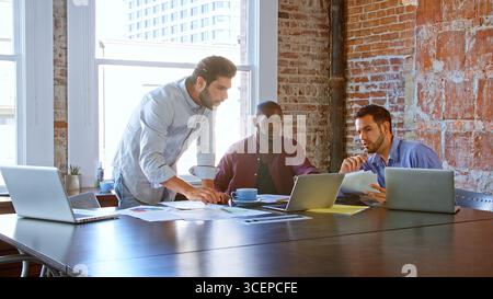Multi-Cultural Group Of Businessmen Working Together Using Laptops In Boardroom Stock Photo