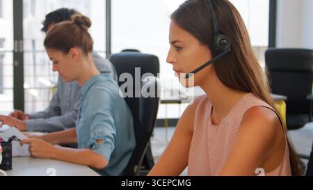 Businesswoman Wearing Headset Sitting At Desk In Office Using Computer Stock Photo