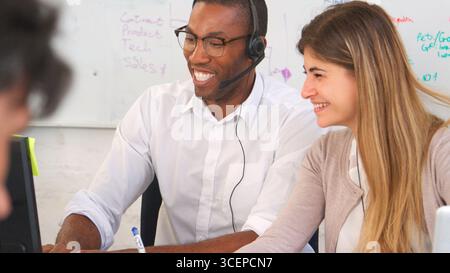 Businessman Wearing Headset And Businesswoman Sitting At Desk In Office Using Computer Stock Photo