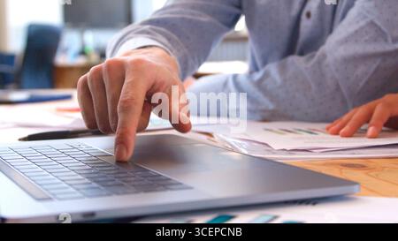 Close Up Of Businessman Sitting At Desk With Finger On Keyboard Of Laptop Stock Photo