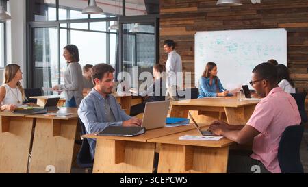 Business Team Sitting At Desks In Open Plan Office Working At Laptops Stock Photo