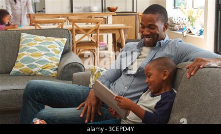 Father And Son At Home Sitting On Sofa In Lounge Using Digital Tablet Stock Photo