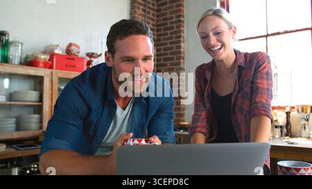 Young Couple Using Laptop In Open Plan Apartment Kitchen Stock Photo