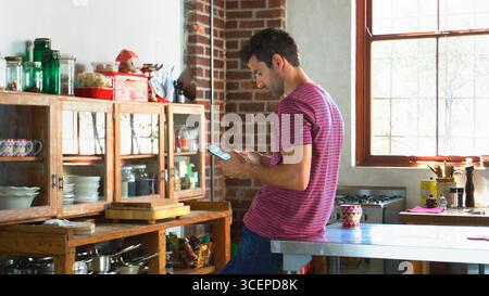 Young Man Using Digital Tablet In Open Plan Apartment Kitchen Stock Photo