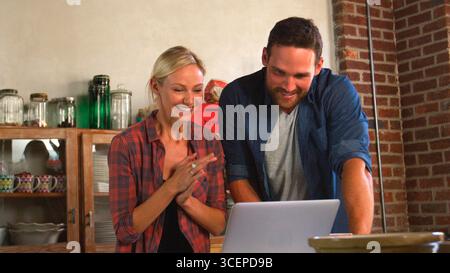 Young Couple Using Laptop In Open Plan Apartment Kitchen Stock Photo