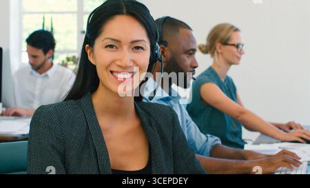Businesswoman Working In Multi-Cultural Team Wearing Headsets In Customer Service Department Stock Photo