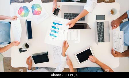 Overhead Shot Of Business Team Meeting Around Table Working On Digital Devices Stock Photo