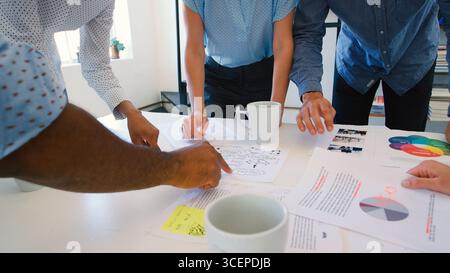 Close Up Of Multi-Cultural Business Team Standing Around Table Discussing Documents In Office Stock Photo