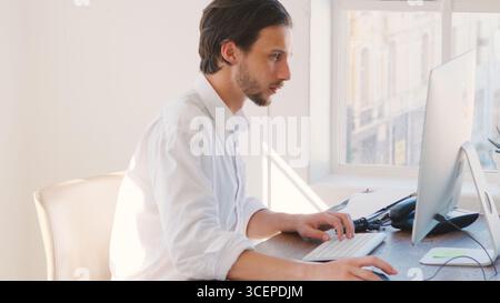 Young Businessman Working At Desk On Computer Talking On Phone Stock Photo