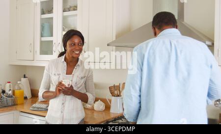 Mature Couple Chat In Kitchen As Man Prepares Meal In Kitchen Stock Photo
