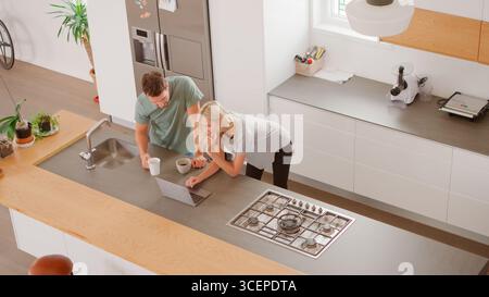Overhead View Of Couple Looking At Laptop In Modern Kitchen Stock Photo