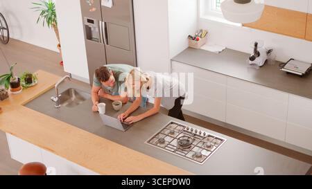 Overhead View Of Couple Looking At Laptop In Modern Kitchen Stock Photo