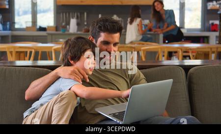 Father And Son Sitting On Sofa In Lounge At Home Using Laptop Together Stock Photo