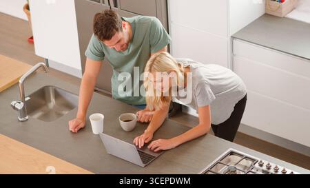 Overhead View Of Couple Looking At Laptop In Modern Kitchen Stock Photo