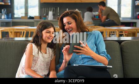 Mother And Daughter Sitting On Lounge Sofa Using Digital Tablet And Laptop Stock Photo