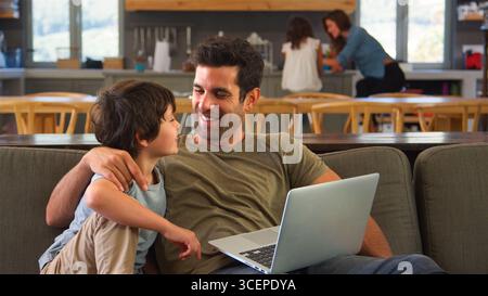 Father And Son Sitting On Sofa In Lounge At Home Using Laptop Together Stock Photo