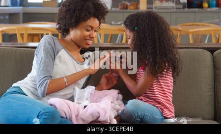 Daughter Sitting On Sofa At Home Painting Mother's Nails Stock Photo