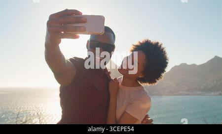 Young Smiling Couple Pose For Holiday Selfie On Clifftop Next To Sea Stock Photo