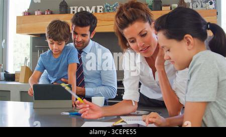 Parents Helping Children With Homework Using Digital Tablet Before Going To Work Stock Photo
