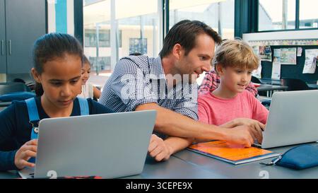 Male High School Teacher With Pupils Using Laptops At Desk In Technology Class Stock Photo