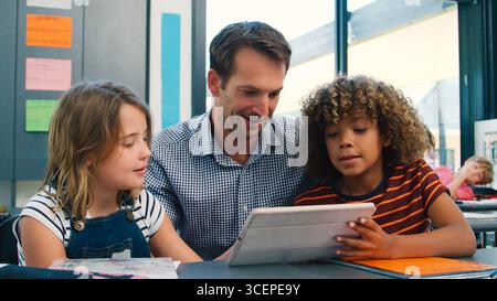 Male High School Teacher With Pupils Using Digital Tablets At Desk In Technology Class Stock Photo