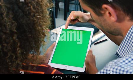 Close Up Of High School Teacher With Male Pupil Using Green Screen Digital Tablet At Desk Stock Photo