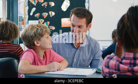 High School Teacher Helping Male Pupil At Desk In Class Stock Photo