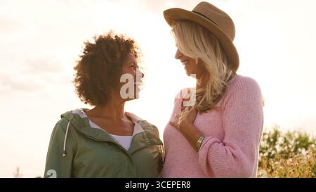 Outdoor Portrait Of Two Smiling Mature Female Friends Against Flaring Sun Stock Photo