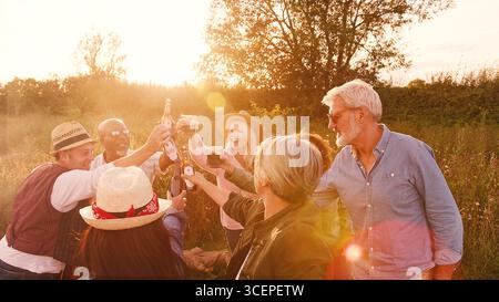 Group Of Mature Friends Making Toast As They Stand Around Fire At Outdoor Campsite Stock Photo