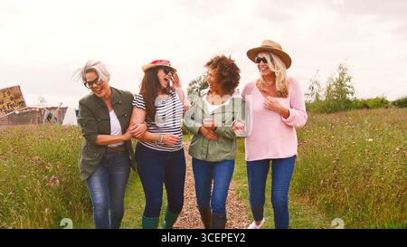 Group Of Smiling Mature Female Friends Walking Arm In Arm Along Path Through Yurt Campsite Stock Photo