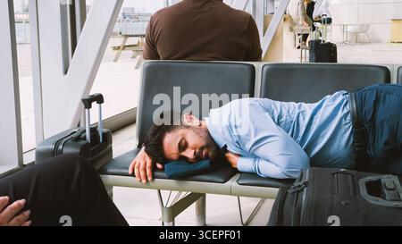 Businessman Sleeping On Seats In Airport Departure Lounge Because Of Delay Stock Photo