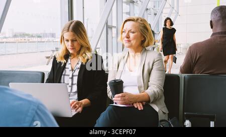 Businesswomen Sitting In Airport Departure Working On Laptop And Drinking Coffee Stock Photo