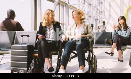Businesswoman Sitting In Airport Departure With Female Colleague In Wheelchair Talking Together Stock Photo