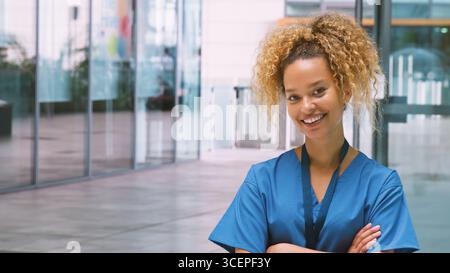 Portrait Of Smiling Female Nurse Wearing Scrubs Standing In Modern Hospital Building Stock Photo