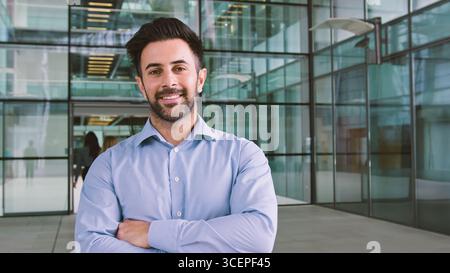 Portrait Of Smiling Businessman Standing In Lobby Of Busy Modern Office Stock Photo