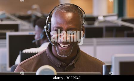 Mature Businessman Wearing Telephone Headset Working In Customer Services Department Stock Photo