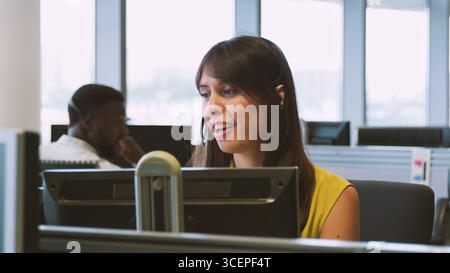 Young Businesswoman Wearing Telephone Headset Working In Customer Services Department Stock Photo
