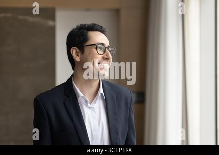 Portrait smiling young businessman standing by office window looking away Stock Photo