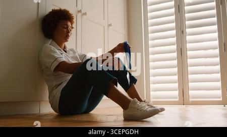 Unhappy And Demotivated Nurse Wearing Uniform Sitting On Floor At Home After Long Shift Stock Photo